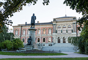 An old big building and a statue of a man in a long coat. Photo.